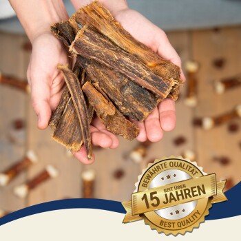 Hände halten große Stücke von Hundekauartikeln, mit einem Abzeichen, das "Beste Qualität" und "15 Jahre bewährte Qualität" auf Deutsch angibt.