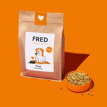Hundetrockenfutterverpackung mit der Aufschrift 'FRED' und einem Cartoonhund, mit den Bezeichnungen 'Pute' und 'Senior', neben einer orangefarbenen Schüssel mit Trockenfutter.