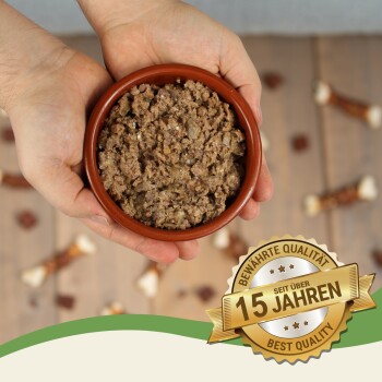 Eine Person hält eine braune Schüssel mit Haustierfutter, umgeben von Hundeleckerlis, mit einem Abzeichen, das "15 Jahre - Beste Qualität" liest.