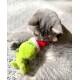 Graue Katze spielt mit einem grünen Grinch-Plüschtier, das einen roten und weißen Weihnachtsmannhut trägt, auf einer strukturierten Oberfläche.