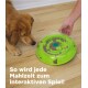Ein Golden Retriever schnüffelt an einer grünen Fressschüssel mit Hundefutter, während eine Hand danach greift. Text: "So wird jede Mahlzeit zum interaktiven Spiel!"