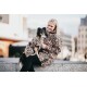 Eine Frau und ihr Hund in passenden Leopardenmuster-Mänteln sitzen auf einer Steinmauer vor einem verschwommenen urbanen Hintergrund.