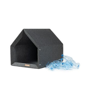 Ein graues Filz-Haustierhaus in Form eines kleinen Hauses, mit einer blauen Plastikflasche in der Nähe, was auf umweltfreundliche Materialien hinweist.