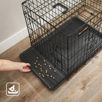 Eine Hand greift nach einer schwarzen Haustierbox mit herausnehmbarem Tablett, auf dem verstreute kleine Haustierleckereien liegen.