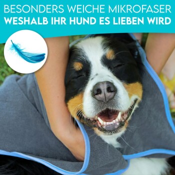 Ein glücklicher Hund in einem weichen Mikrofaserhandtuch, sanft von einer Person gehalten. Text darüber: "Besonders weiche Mikrofaser, weshalb Ihr Hund es lieben wird."