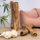 Eine Glasvase enthält große Hundekauartikel, zwei weitere liegen auf einem Holztisch neben einem Seilspielzeug und einem pinken Haustierbett im Hintergrund.
