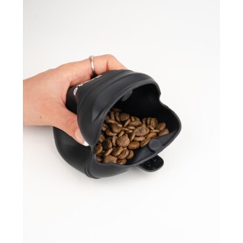 Eine Hand hält einen schwarzen Silikon-Haustierfutterlöffel, gefüllt mit trockenem Futter, vor einem weißen Hintergrund.