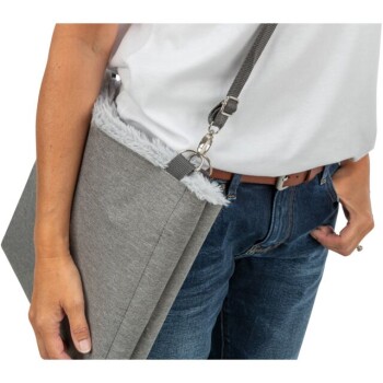Eine Person trägt ein weißes T-Shirt und eine blaue Jeans und hält eine graue Haustiertragetasche mit einem flauschigen oberen Rand und einem Schultergurt.