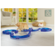 Eine flauschige orangefarbene Katze spielt mit einer blauen, flexiblen Katzen-Spielbahn auf einem hellen Holzboden, mit einem sonnigen Raum und großen Fenstern im Hintergrund.