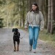 Person in beige Jacke und Jeans führt einen schwarz-braunen Dobermann an der Leine entlang eines kiesigen Waldwegs.