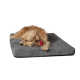 Ein flauschiger Hund schläft friedlich auf einem weichen grauen Haustierbett und hält ein kleines Plüschspielzeug mit einem roten Hut.