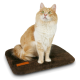 Eine flauschige orange-weiße Katze sitzt auf einem braunen Haustierbett und schaut mit leuchtend grünen Augen nach oben. Das Bett hat ein kleines oranges Etikett.