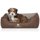 Ein kleiner, flauschiger Hund sitzt bequem in einem stilvollen braunen Haustierbett mit einem hellen Innenraum, mit dem Logo "KNUFFELWUFF".