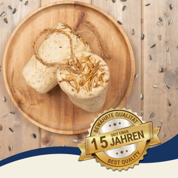 Zwei zylindrische Vogelfutterblöcke mit getrockneten Insekten auf einem Holzbrett, umgeben von Sonnenblumenkernen und einem "Best Quality - 10 Years" Abzeichen.