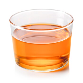 Ein klares Glas, gefüllt mit orangefarbigem Flüssigkeit, das Licht reflektiert, vor einem weißen Hintergrund.