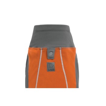 Eine Nahaufnahme einer Hundejacke mit einem grauen Oberteil und einem orangen Fleece-Unterteil, mit einem Ruffwear-Logo und reflektierenden Nähten.