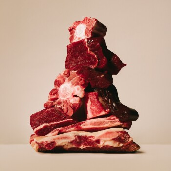 Pile de viande rouge crue et d'os à moelle avec centres osseux exposés sur fond beige.