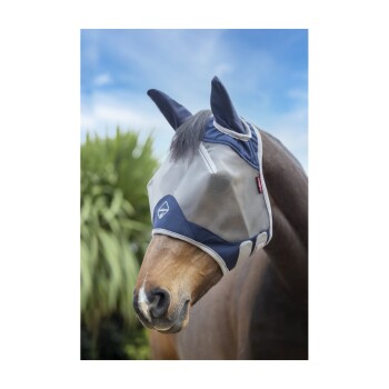 Ein braunes Pferd mit einer schützenden Fliegenmaske mit marineblauen Akzenten, vor einem hellen Himmel und grünem Laub.