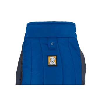 Eine blaue Hundejacke mit einem gesteppten Design, die ein Ruffwear-Logo-Patch eines Hundes auf gelbem Hintergrund zeigt.