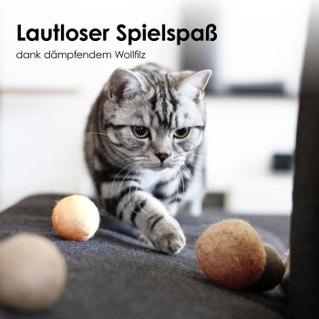 Eine dreifarbige Katze kuschelt friedlich mit einem weichen, pfirsichfarbenen Filzball, wobei der Text "Natürliches Material" und "Katzen lieben Wollfilz" sichtbar ist.