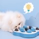 Ein flauschiger weißer Hund interagiert mit einem blauen Puzzlespielzeug, das für Haustiere entworfen wurde, mit einer Sprechblase, die ein Glühbirnen- und Gehirn-Icon zeigt.