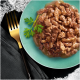 Gros plan d'une assiette turquoise remplie de viande humide et effilochée dans une sauce, garnie d'une branche de persil, à côté d'une fourchette dorée sur une serviette sombre.