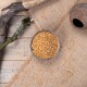 Eine Holzschüssel, gefüllt mit kleinen, goldenen Körnern, steht auf einem Jutesack, umgeben von verstreuten Samen und einem rustikalen Ast.