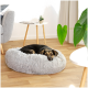 Ein schwarz-brauner Hund ruht auf einem flauschigen grauen Hundebett in einem gemütlichen Wohnzimmer, mit einer kleinen Pflanze und einem Beistelltisch in der Nähe.