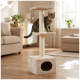 Getigerte Katze sitzt auf der mittleren Plattform eines beigen mehrstöckigen Kratzbaums mit Pompon-Spielzeug und Höhle in einem sonnendurchfluteten Wohnzimmer.