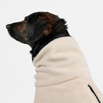 Ein Seitenprofil eines Hundes, der einen weichen, beigen Fleece-Mantel trägt, der sein schwarz-braunes Fell und seinen aufmerksamen Ausdruck zeigt.