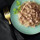 Gros plan sur une assiette vert clair avec de la nourriture pour animaux en gelée, garnie de persil, et une fourchette dorée sur un fond sombre.