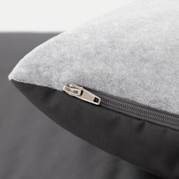 Nahaufnahme einer Ecke eines Haustierbettes mit einer grauen Fleece-Oberseite und einem schwarzen Stoffboden, mit einem sichtbaren Reißverschluss für einfache Reinigung.