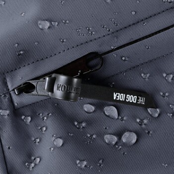 Nahaufnahme eines wasserdichten Hundejackenreißverschlusses mit Wassertropfen auf einem dunkelgrauen Stoff, mit einem Etikett, das 'THE DOG IDEA' liest.