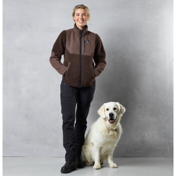 Eine Person in einer braunen Fleecejacke und schwarzen Hosen steht neben einem lächelnden Golden Retriever vor einem grauen Hintergrund.