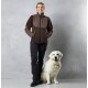 Eine Person in einer braunen Fleecejacke und schwarzen Hosen steht neben einem lächelnden Golden Retriever vor einem grauen Hintergrund.