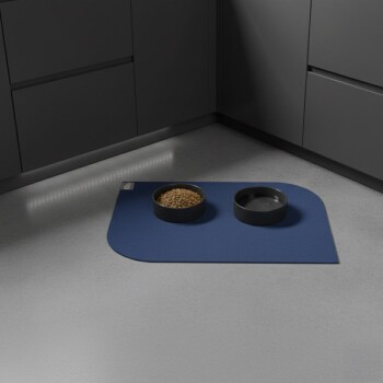 Schwarze Futter- und Wassernäpfe auf einer blauen Matte in einer Küchenecke mit grauen Schränken.