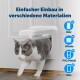 Eine grau-weiße Katze verlässt eine weiße Katzenklappe in einer Holztür. Text lautet "Einfacher Einbau in verschiedene Materialien" mit Kompatibilitätssymbolen.