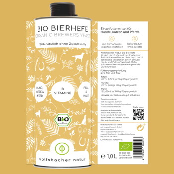 Eine Frau mit einer schwarzen Katze sitzt neben einem wolfähnlichen Hund in einem Garten mit lila Blumen. Text: "Als Haustierheilerin liebe ich Wolfsbacher Naturprodukte."
