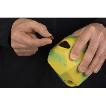 Eine Person hält ein buntes gelb-grünes Haustierspielzeug in einer Hand, während sie mit der anderen Hand einen kleinen Haustier-Leckerbissen anbietet.