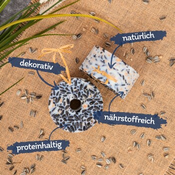 Zwei dekorative Vogelfutterkuchen auf einem Jutesack-Hintergrund, beschriftet mit 'dekorativ', 'natürlich', 'nährstoffreich' und 'proteinhaltig.'