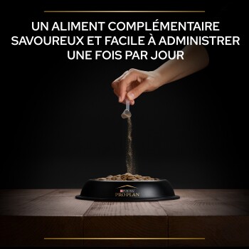 Une main verse de la poudre dans un bol noir de nourriture sèche pour animaux, avec un texte au-dessus : "UN ALIMENT COMPLÉMENTAIRE SAVOUREUX ET FACILE À ADMINISTRER."