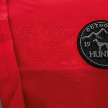 Nahaufnahme einer roten wasserdichten Hundejacke mit Wassertropfen auf der Oberfläche und einem runden schwarzen Patch, auf dem "OUTDOOR HUNT 19" steht.