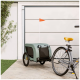 Ein grüner Haustieranhänger mit einem schwarzen Netzfenster und einer orangefarbenen Fahne, der neben einem Fahrrad auf einem Steinweg in der Nähe einer Garage geparkt ist.