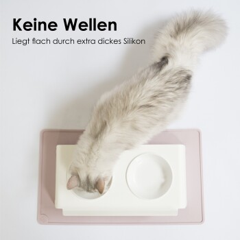 Eine flauschige hellgraue Katze frisst aus einer weißen Schüssel auf einer rosa Matte mit dem Text: "Keine Wellen" und "Liegt flach durch extra dickes Silikon."