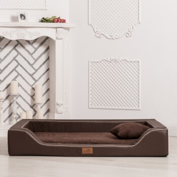 Ein stilvolles braunes Haustierbett mit einem plüschigen Kissen und einem kleinen Kissen, vor einer minimalistischen weißen Wand und einem eleganten Kamin.