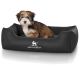 Ein kleiner, flauschiger Welpe sitzt bequem in einem schwarzen Hundebett mit dem Logo "KNUFFELWUFFF", das prominent auf der Vorderseite angezeigt wird.