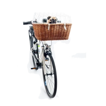 Un vélo blanc avec un panier en osier brun à l'avant, contenant un chien carlin qui regarde par derrière une cage en métal.