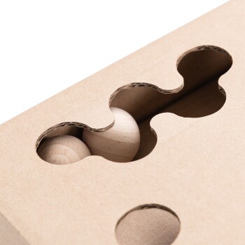 Nahaufnahme eines Puzzlespielzeugs aus Pappe mit runden Ausschnitten, die zwei Holzkugeln im Inneren zeigen, entworfen für die Beschäftigung von Haustieren.