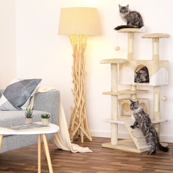 Drei flauschige Katzen spielen auf einem beigen Katzenbaum in einem gemütlichen Wohnzimmer, das eine stilvolle Lampe und ein graues Sofa mit dekorativen Kissen zeigt.