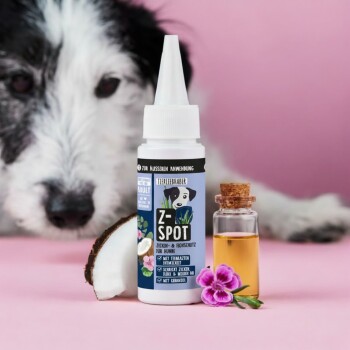 Flasche des Haustierprodukts 'Z-Spot für Hunde' auf einem rosa Hintergrund, begleitet von einem kleinen Glasfläschchen mit Öl, einer Kokosnuss-Scheibe und Blumen.